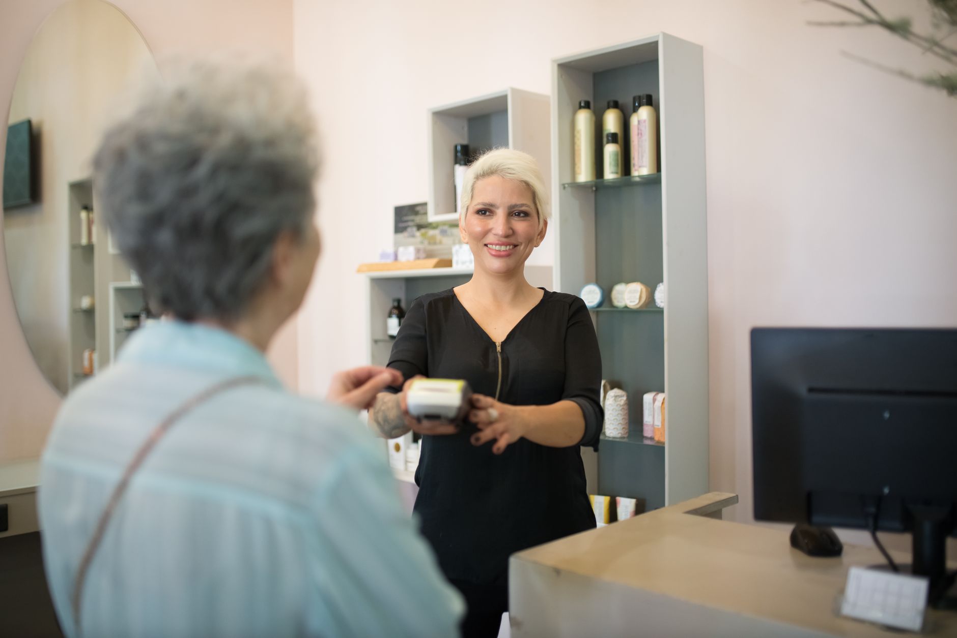 coiffeuse souriante encaissant une cliente aux cheveux gris au comptoir d'un salon