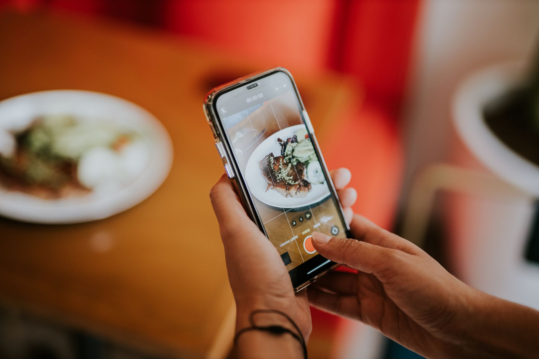 mains tenant un smartphone qui photographie une assiette posée sur une table de restaurant