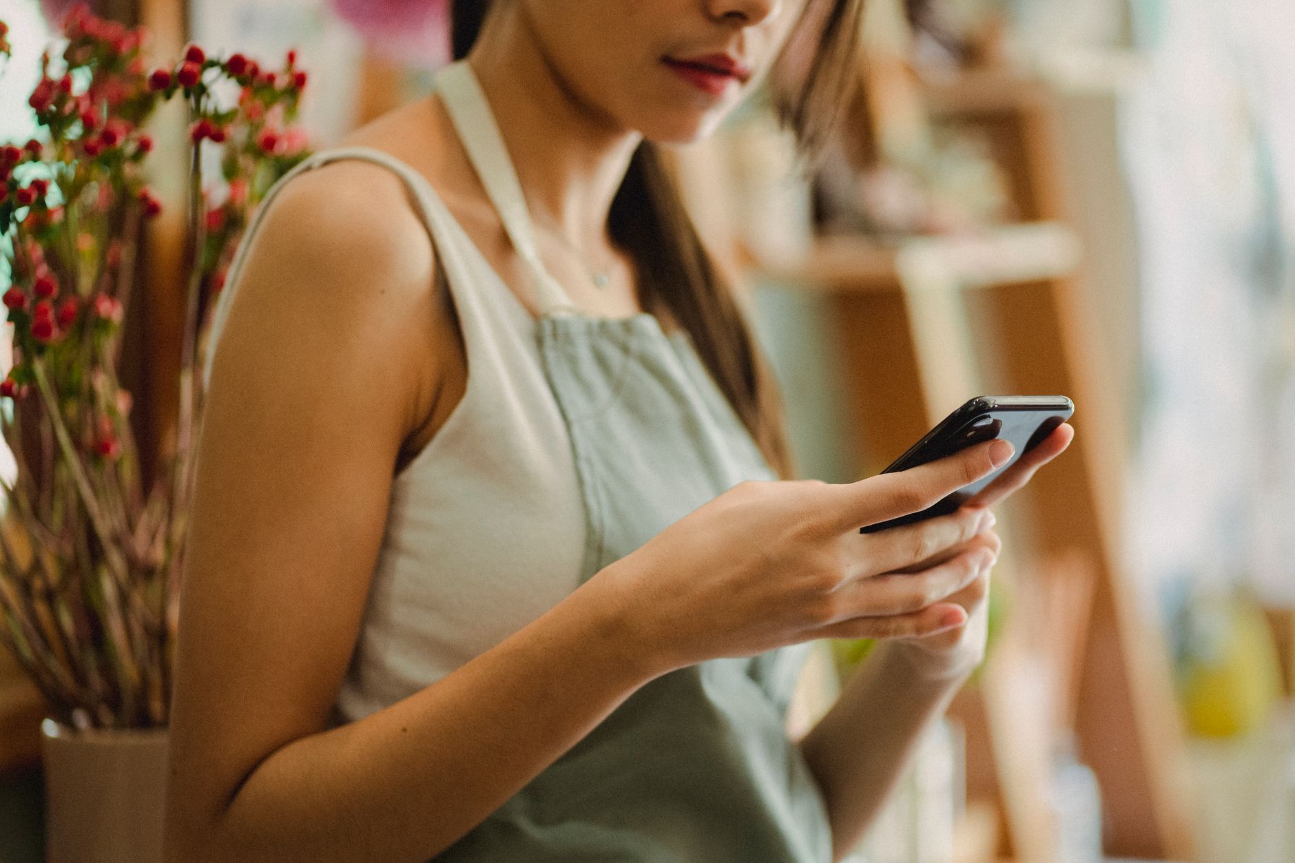 commerçante en tablier consultant son smartphone dans sa boutique de fleurs